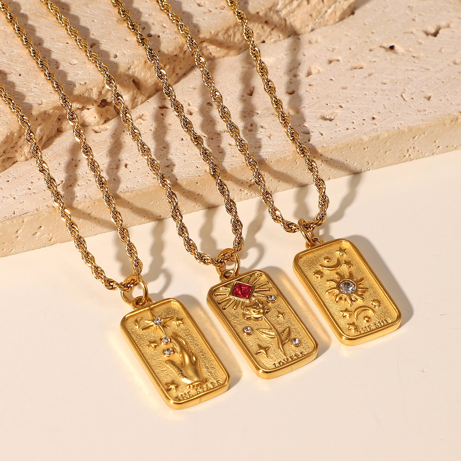 Three gold necklaces with tarot card pendants on a textured beige surface - from Aurie Jewelry bestie collection 